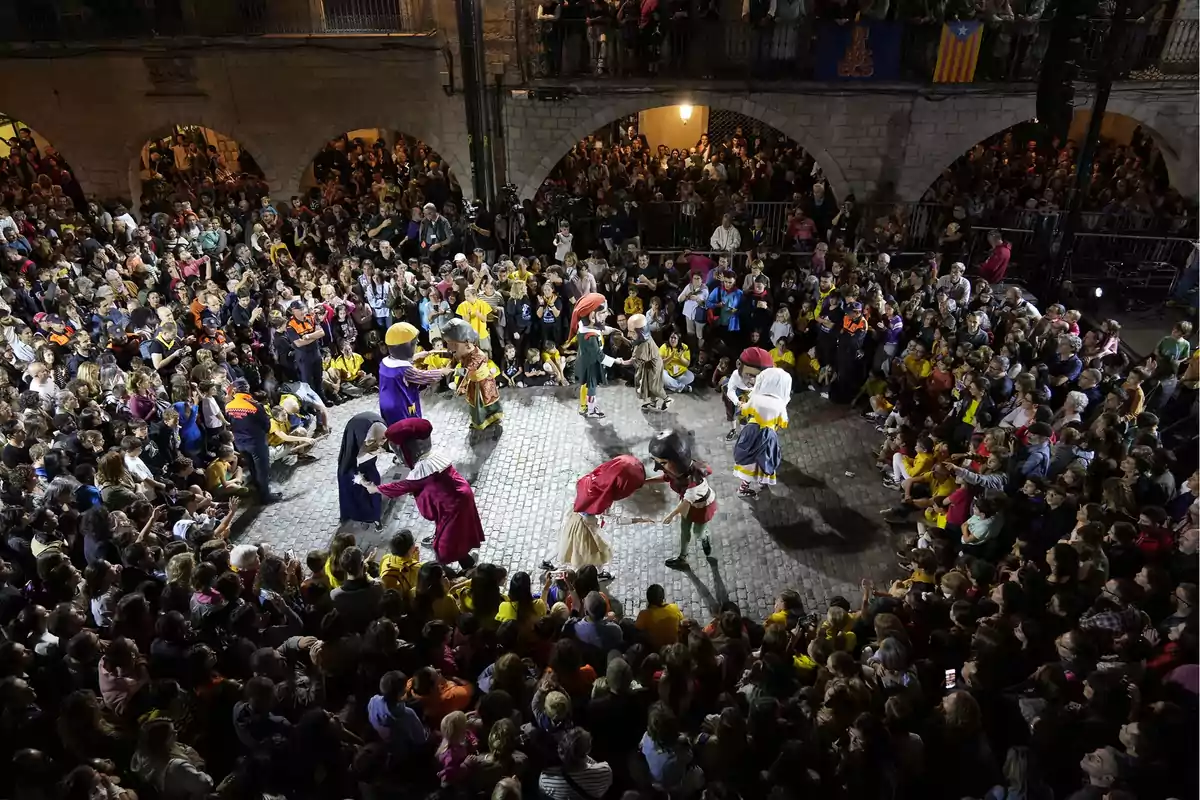 Una multitud observa un espectáculo de personas disfrazadas con cabezudos en una plaza iluminada por la noche.