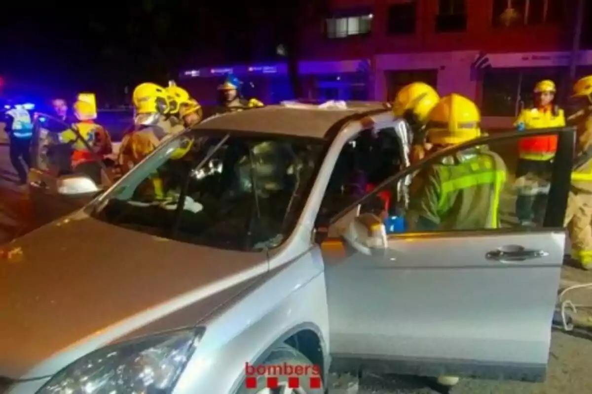 Bomberos trabajando en la escena de un accidente de tráfico con un coche plateado involucrado.