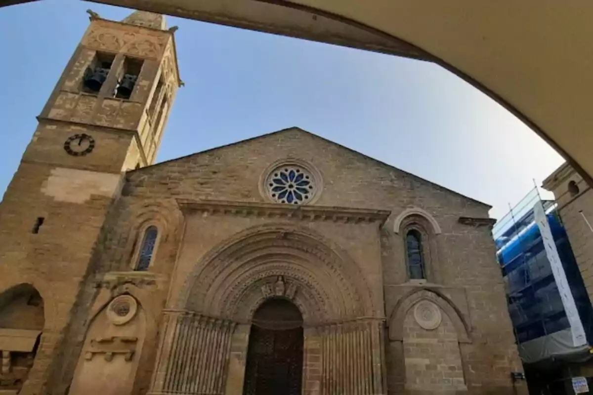 Fachada de una iglesia de piedra con un campanario y un reloj, con un cielo despejado de fondo.