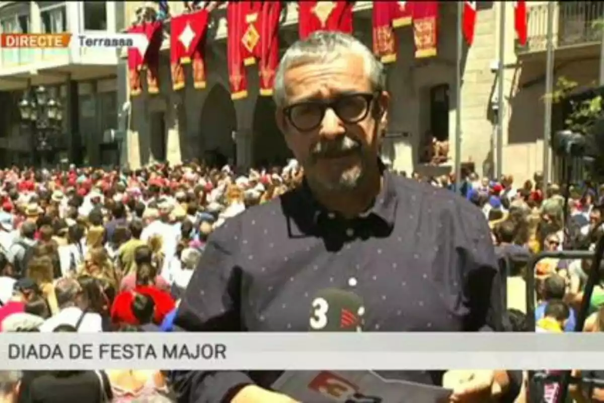 Un reportero cubre un evento multitudinario en una plaza decorada con banderas rojas durante la Diada de Festa Major en Terrassa.