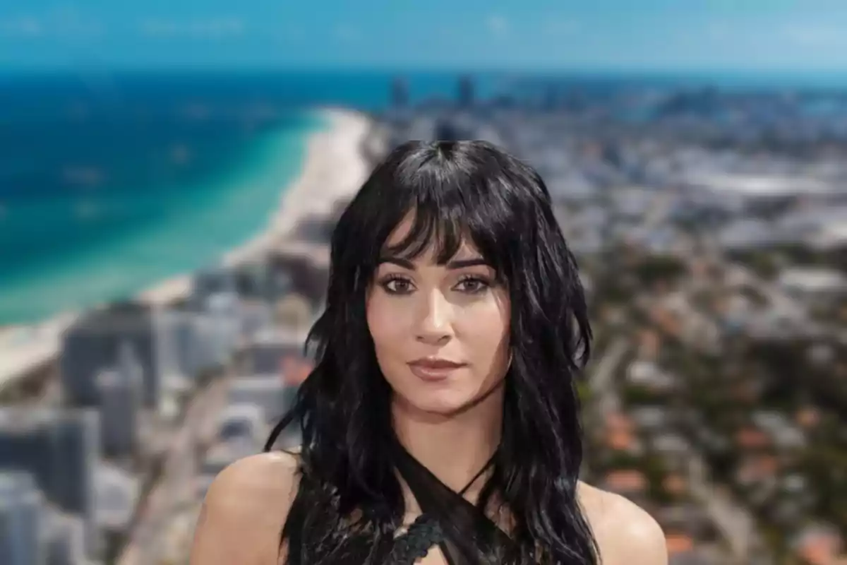 Una mujer de cabello oscuro con un fondo de playa y ciudad desenfocado.