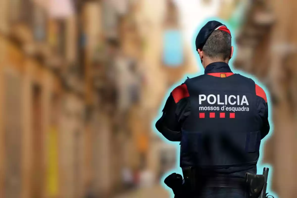 Un agente de policía de espaldas con uniforme de los Mossos d'Esquadra en una calle desenfocada.