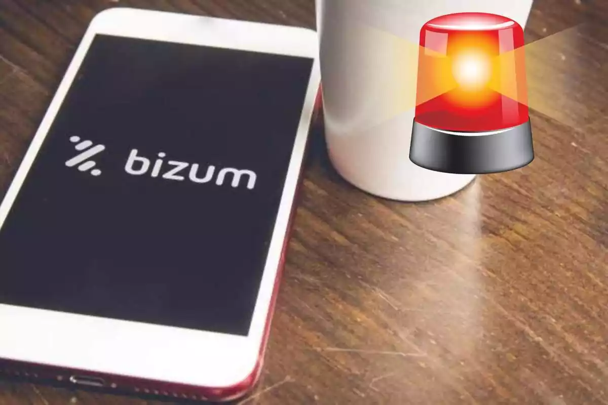 Montaje con smartphone con la palabra y el logo de Bizum encima de una mesa. Señal de emergencias en la parte superior derecha