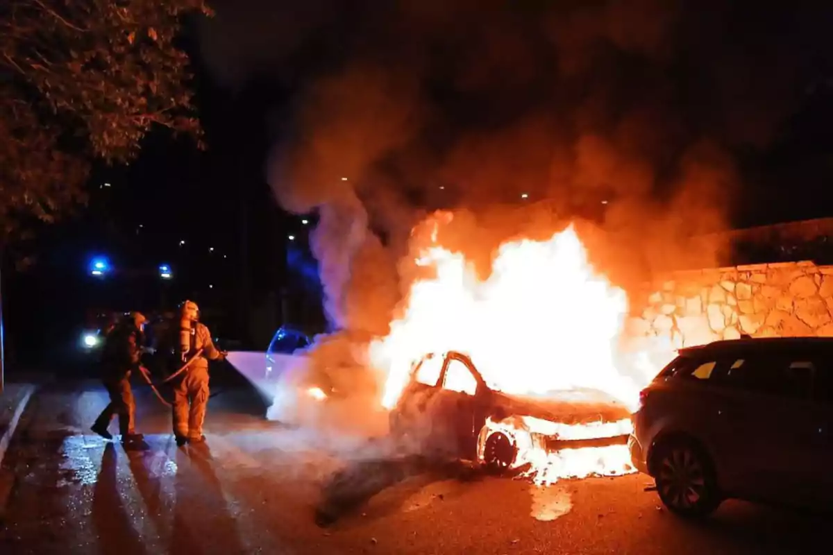 Bomberos apagando un coche en llamas durante la noche.