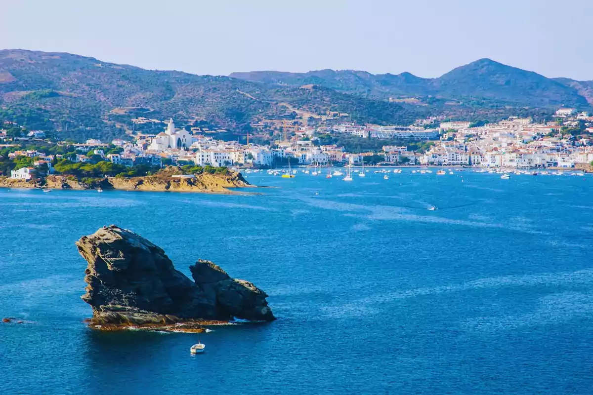 Vista panorámica de un pueblo costero con un mar azul y una formación rocosa en primer plano.