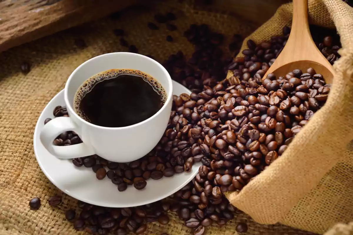 Taza de café negro junto a un saco de granos de café sobre una superficie de arpillera.