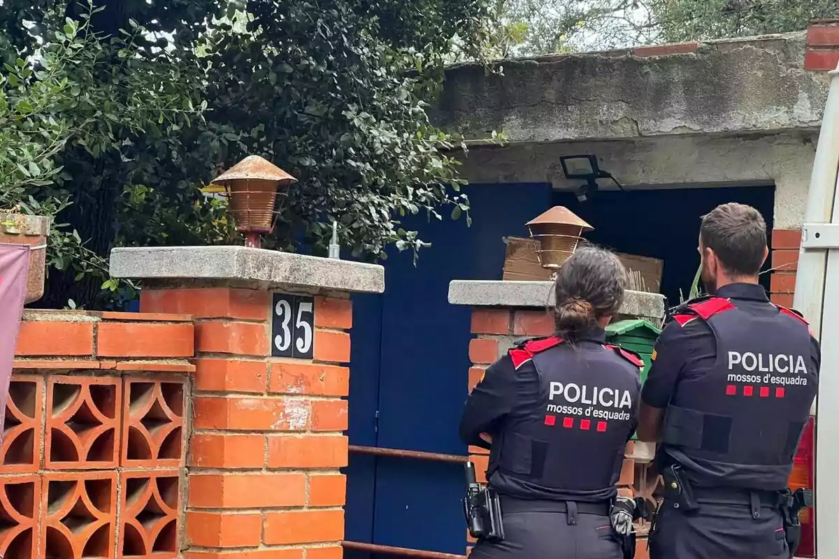 Dos agentes de policía de los Mossos d'Esquadra de espaldas frente a una casa con el número 35 en la entrada.