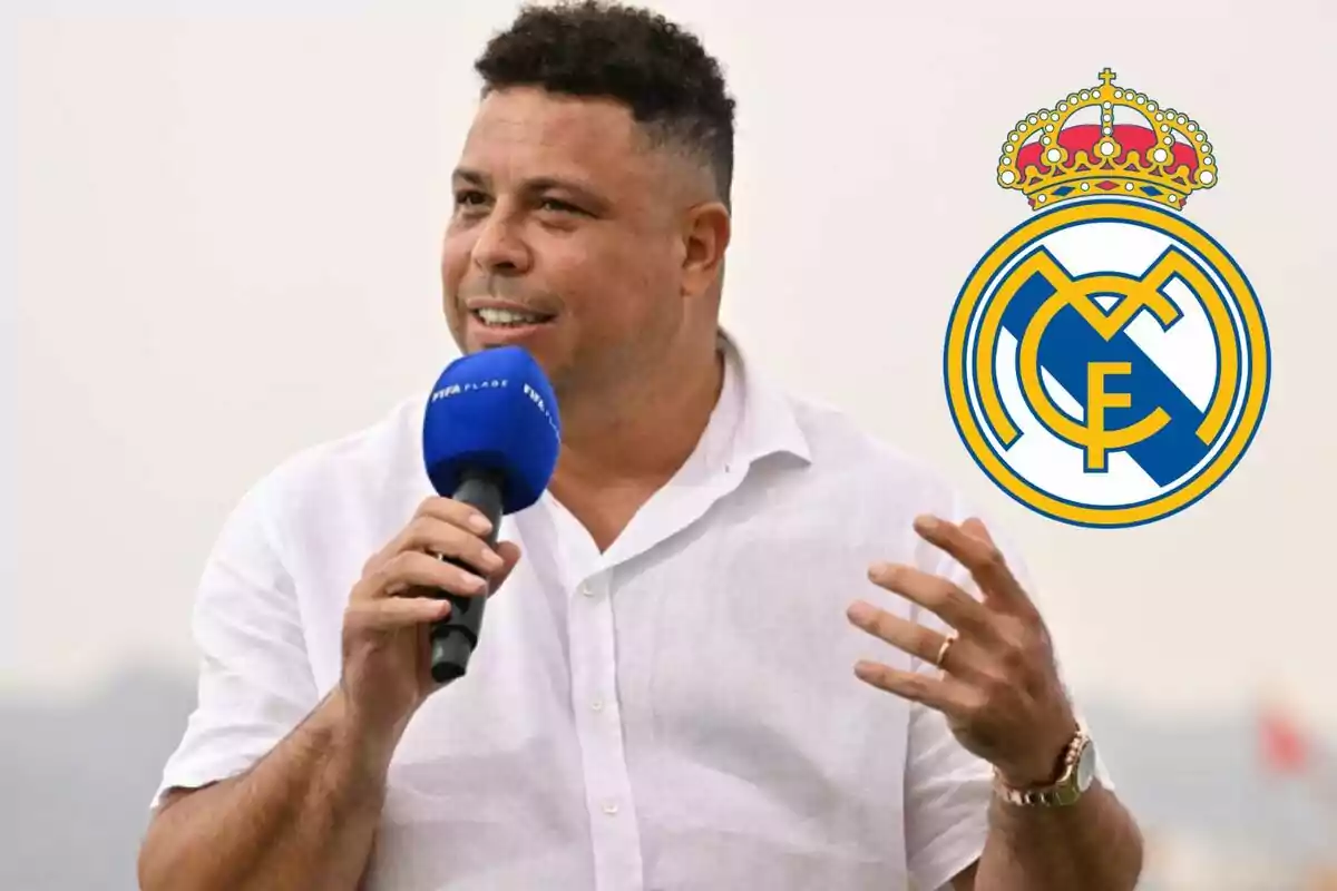 Hombre hablando con un micrófono azul de FIFA y el logo del Real Madrid a su lado.