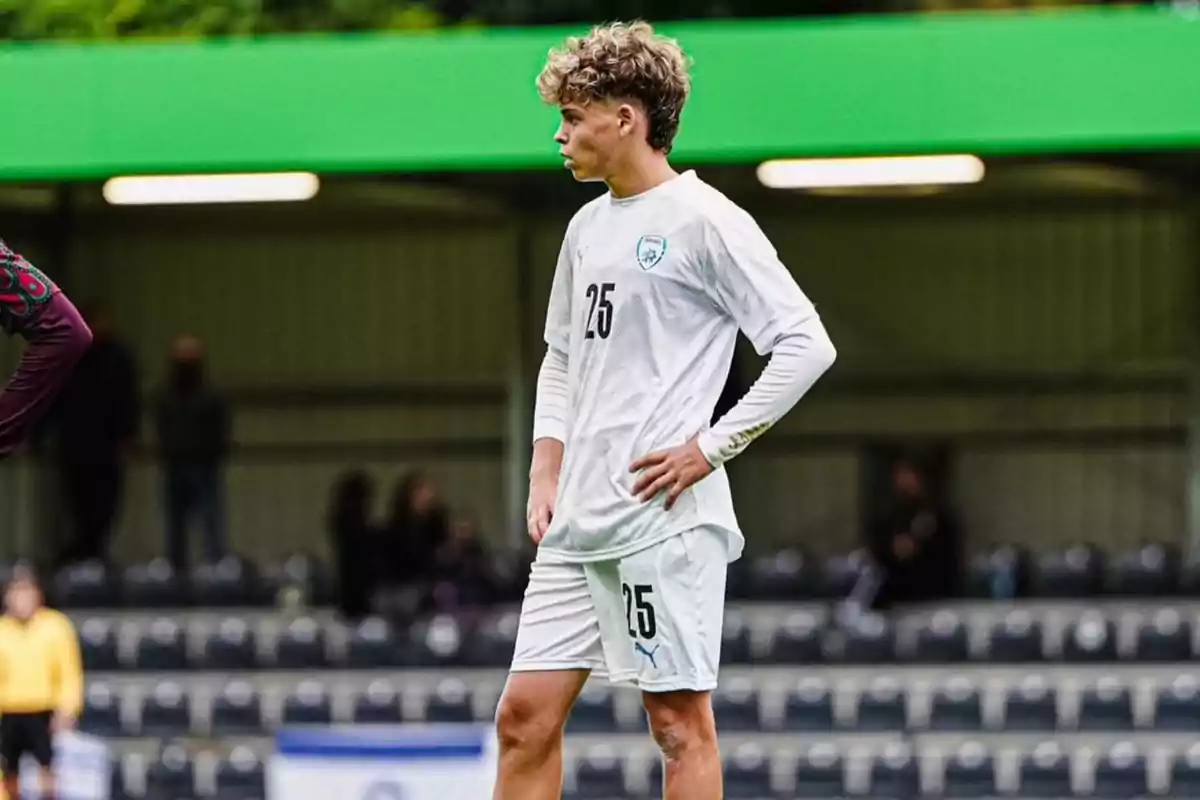 Un jugador de fútbol con el uniforme blanco número 25 está de pie en el campo durante un partido.