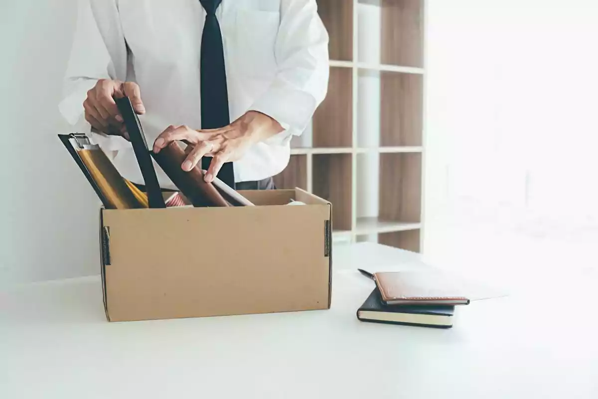 Persona empacando objetos personales en una caja de cartón sobre un escritorio.