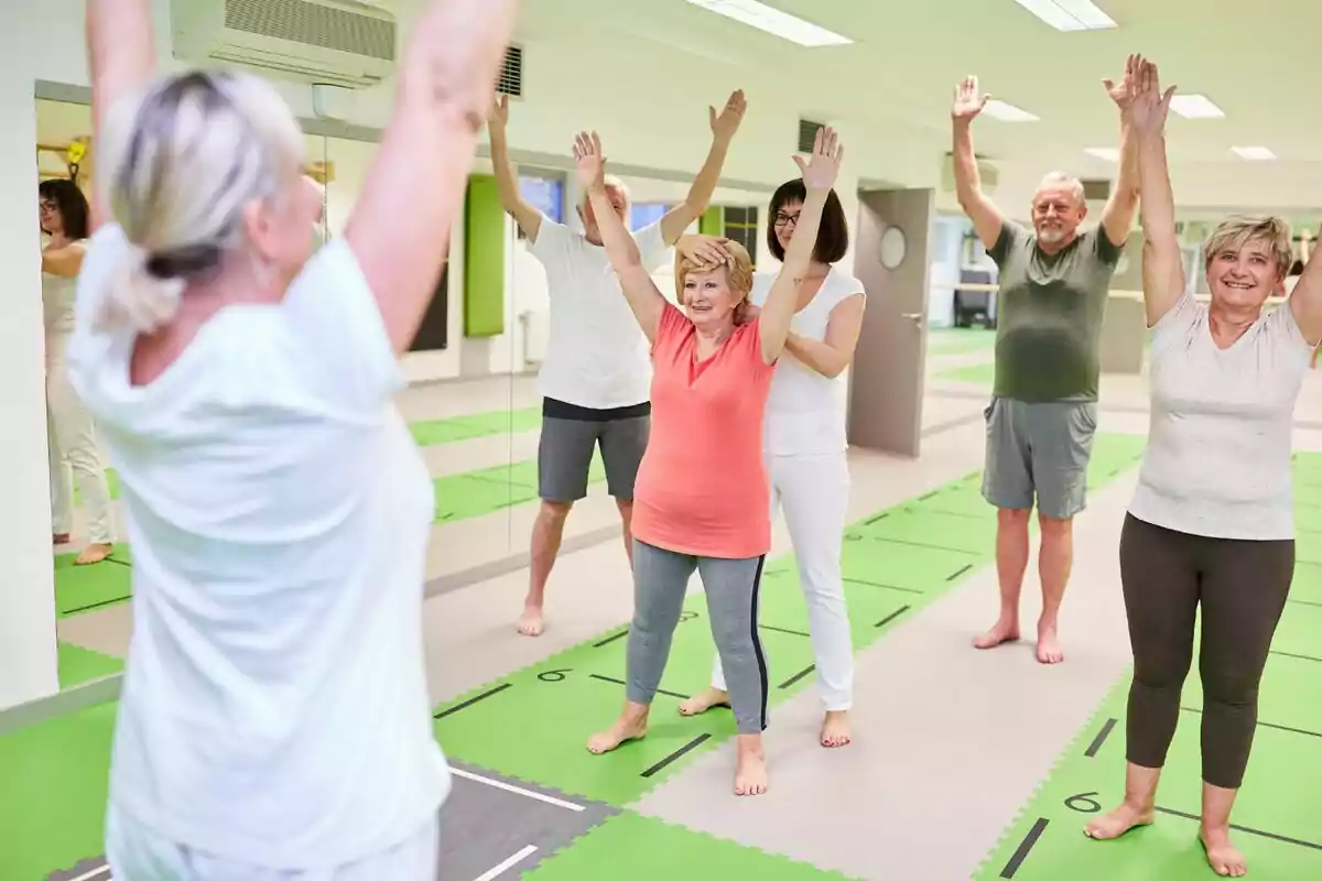 Personas mayores haciendo ejercicios de estiramiento en una clase grupal en un gimnasio.