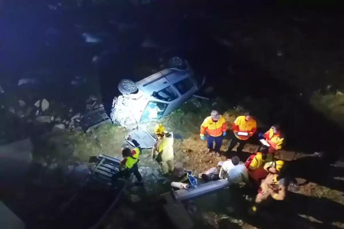 Rescatistas trabajando en el lugar de un accidente automovilístico con un coche volcado en un área oscura.