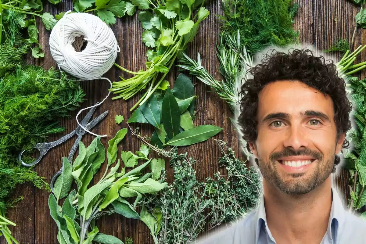 Un hombre sonriente con cabello rizado y barba, rodeado de diversas hierbas frescas, tijeras y un rollo de hilo sobre una superficie de madera.