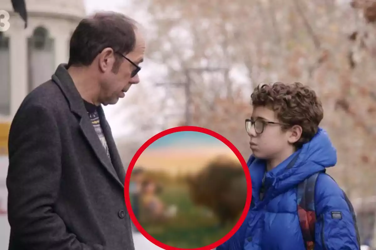 Un hombre y un niño con gafas están conversando al aire libre, el hombre lleva un abrigo gris y el niño una chaqueta azul, en el centro de la imagen hay un círculo rojo con una imagen borrosa dentro.