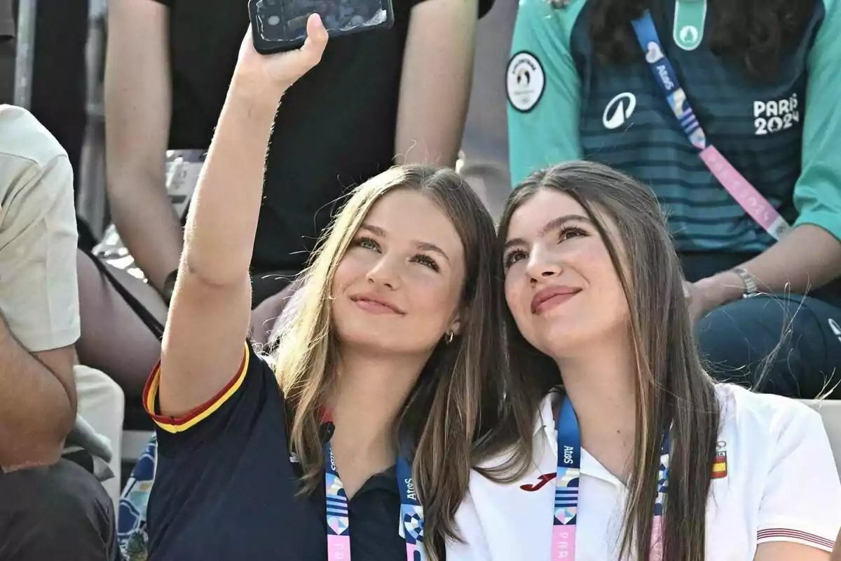 Dos jóvenes se toman una selfie mientras asisten a un evento deportivo, ambas llevan colgadas acreditaciones y una de ellas viste una camiseta con los colores de la bandera de España.