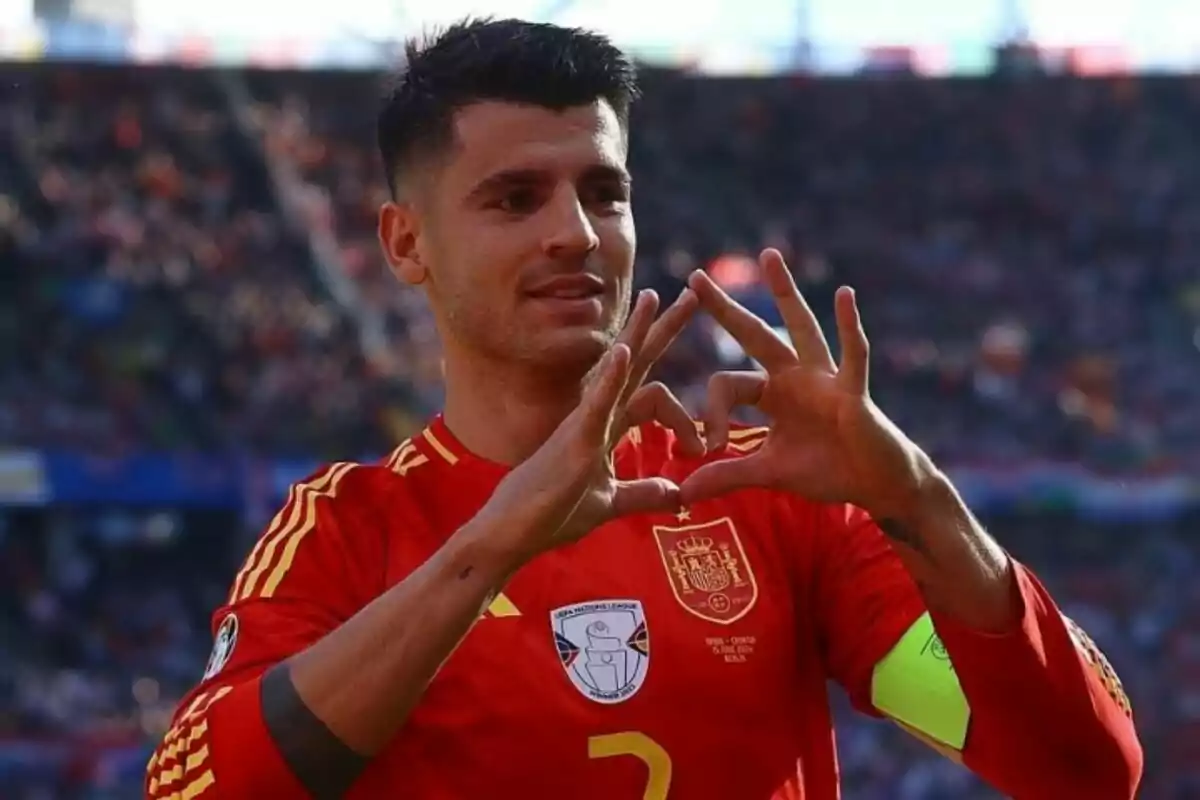 Un jugador de fútbol con la camiseta de la selección española hace un gesto de corazón con las manos en un estadio.