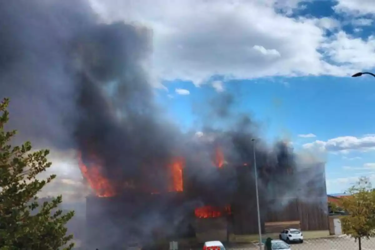 Edificio en llamas con una gran cantidad de humo negro bajo un cielo parcialmente nublado.