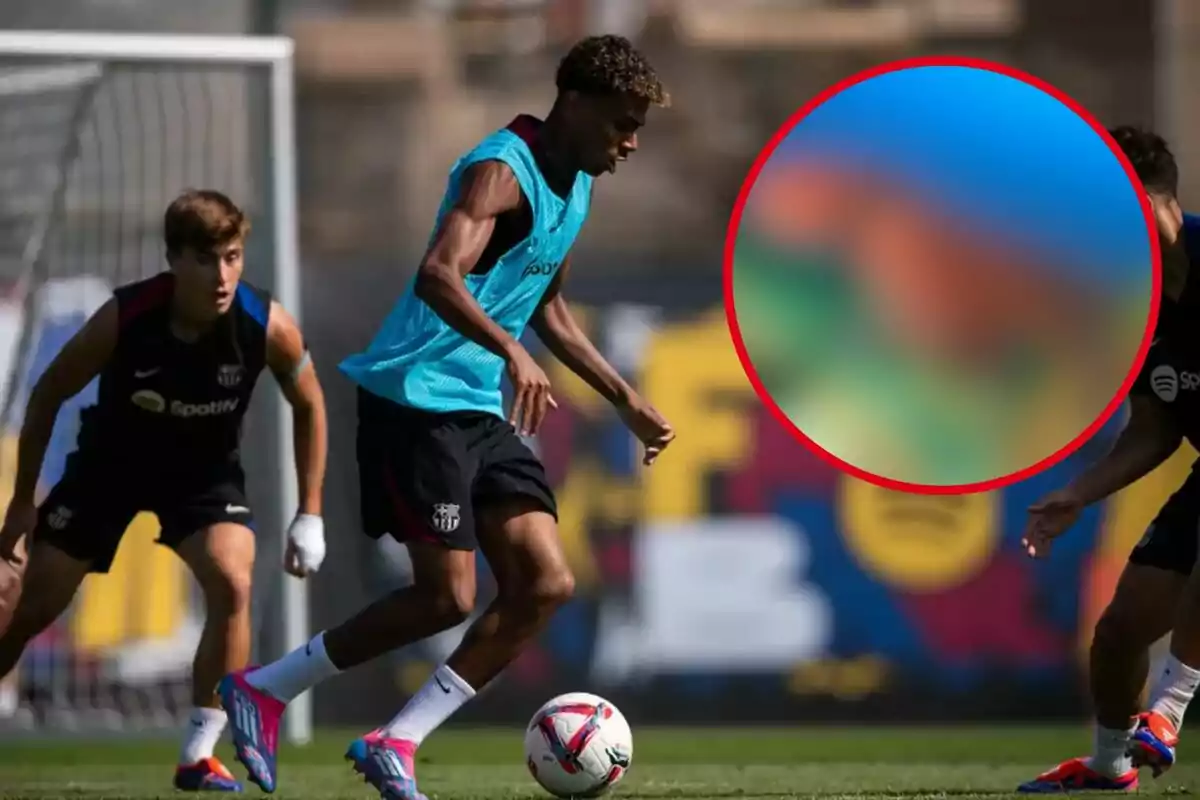 Jugadores de fútbol entrenando en un campo, uno de ellos lleva un peto azul y está controlando el balón mientras otros dos jugadores observan.