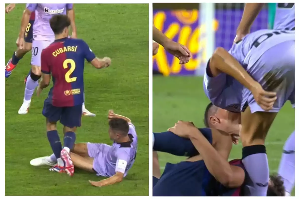 Jugadores de fútbol en el suelo durante un partido, uno de ellos ayuda al otro a levantarse.