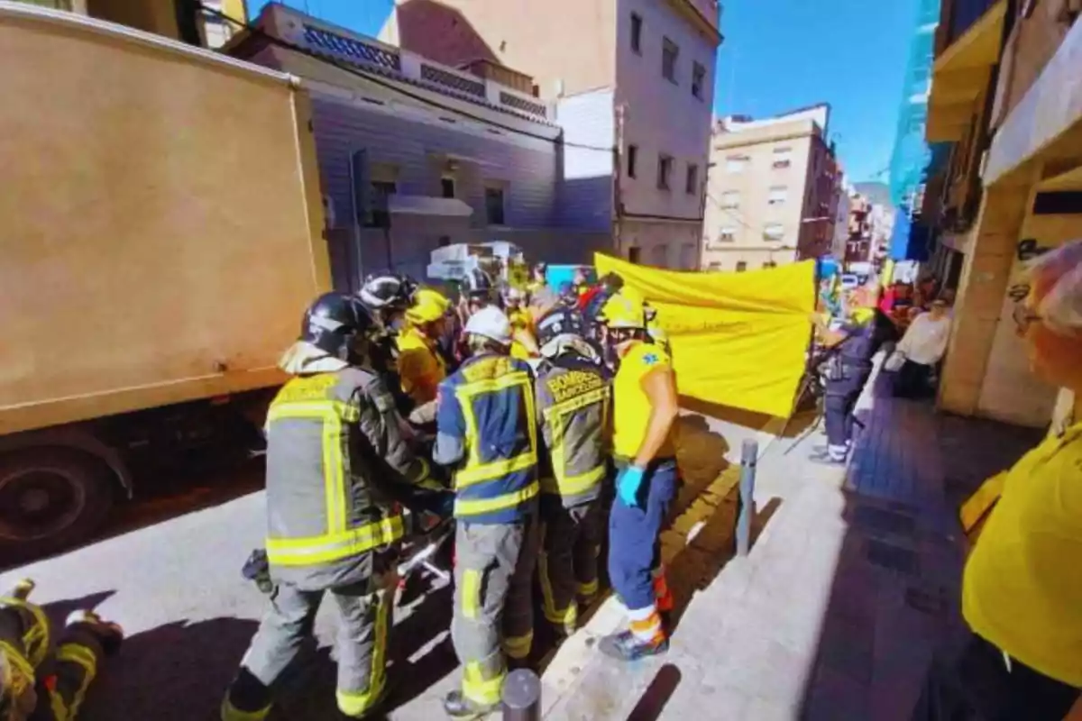 Bomberos y personal de emergencia trabajando en una calle junto a un camión, con un grupo de personas observando.