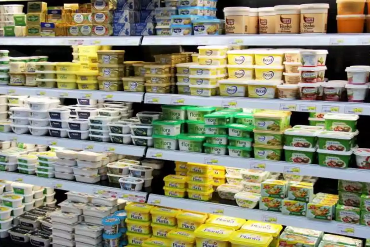 Estantes de supermercado llenos de diferentes marcas y tipos de margarina y mantequilla en envases de plástico.