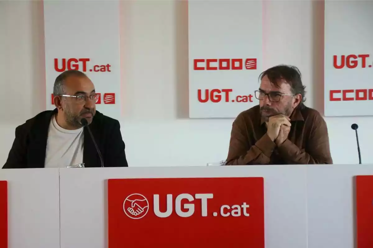 Dos hombres sentados en una mesa con micrófonos, con logotipos de UGT.cat y CCOO en el fondo.