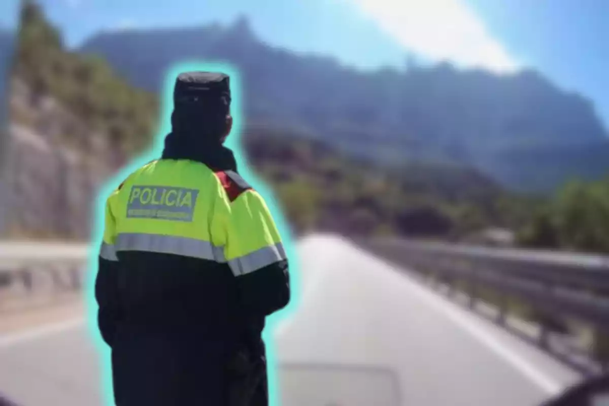 Un policía con uniforme amarillo y negro de espaldas en una carretera con montañas al fondo.