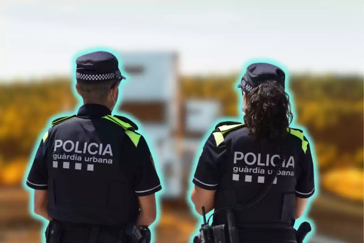 Dos agentes de la policía urbana de espaldas, con uniformes oscuros y detalles reflectantes, observan un vehículo borroso al fondo en un entorno al aire libre.