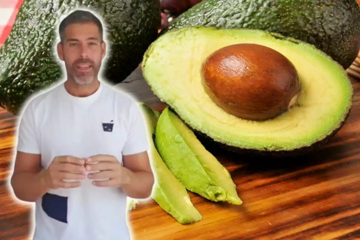 Hombre con camiseta blanca frente a una imagen de aguacates sobre una mesa de madera.