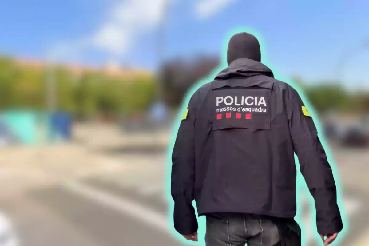 Policía de los Mossos d'Esquadra de espaldas con uniforme negro en un entorno urbano desenfocado.