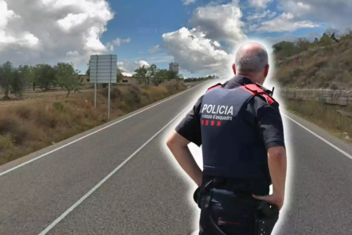 Un policía de los Mossos d'Esquadra de espaldas en una carretera rural bajo un cielo parcialmente nublado.