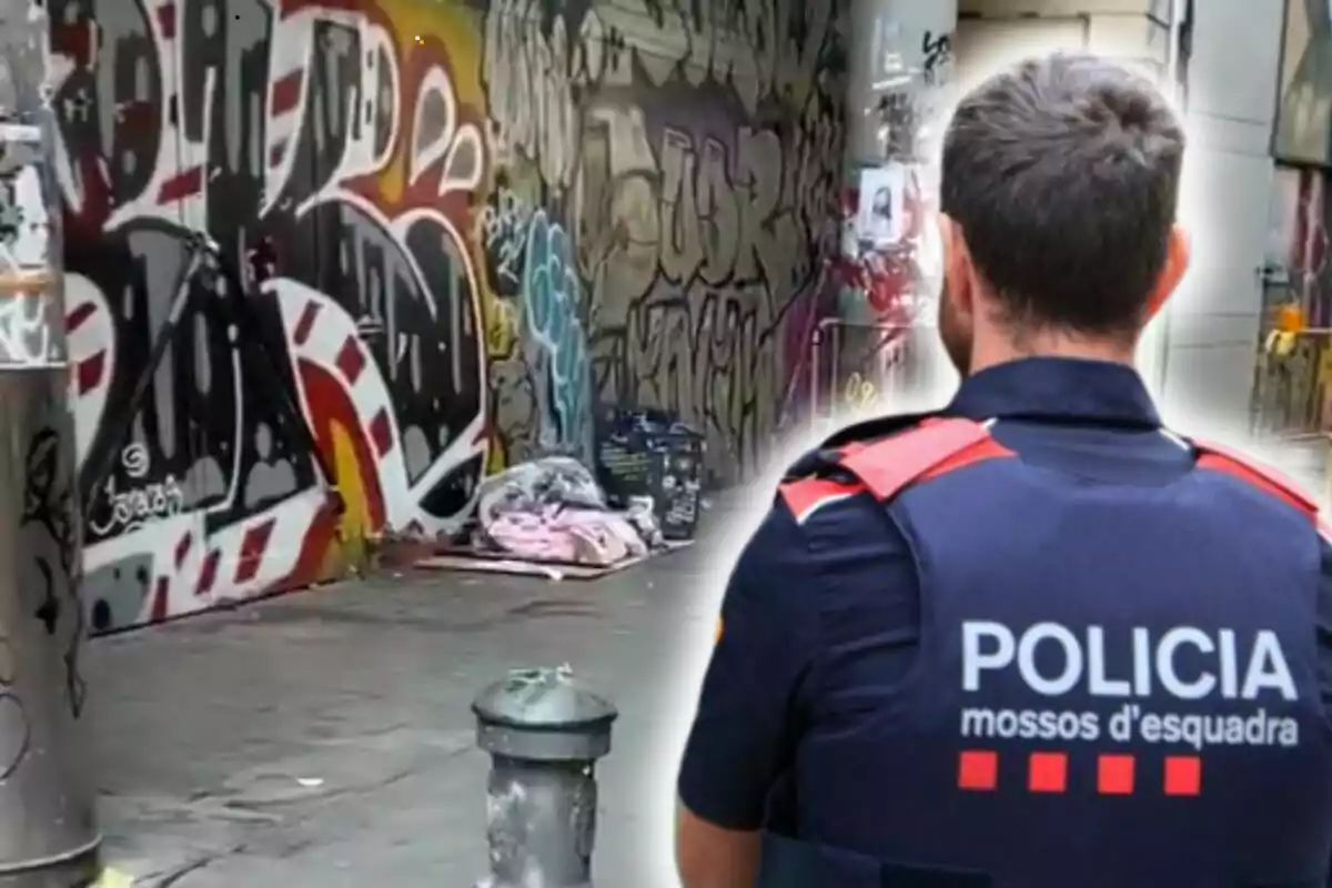 Un agente de policía de espaldas observa una calle con grafitis y una persona durmiendo en el suelo.