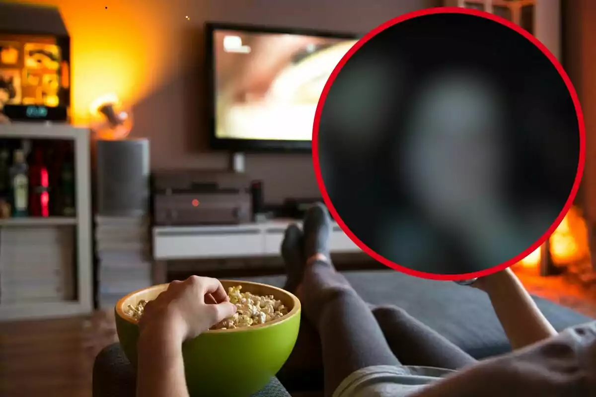 Una persona está recostada en un sofá viendo televisión y comiendo palomitas de maíz en una sala de estar acogedora.