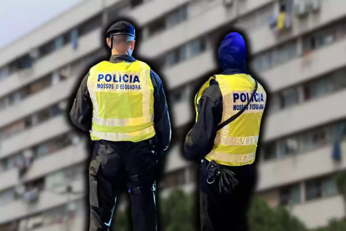 Dos agentes de policía con chalecos reflectantes de los Mossos d'Esquadra de espaldas frente a un edificio residencial.