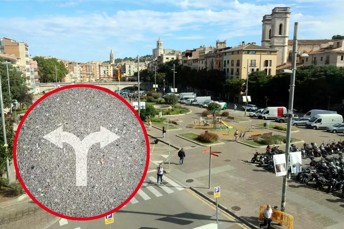 Vista aérea de una plaza urbana con un parque infantil, estacionamiento de motocicletas y varios edificios al fondo, con un círculo rojo que contiene una señal de tráfico indicando una bifurcación.