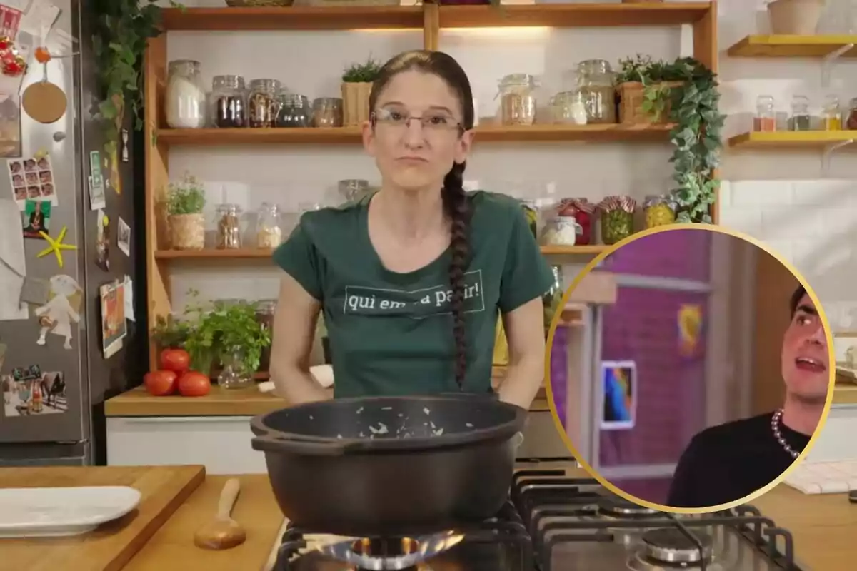 Una mujer con una trenza larga y gafas está en una cocina, frente a una estufa con una olla negra, mientras que en la esquina inferior derecha hay un recuadro con la imagen de otra persona.