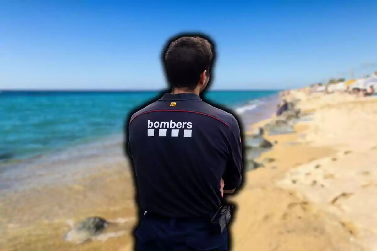 Un bombero de espaldas en la playa con el mar de fondo.