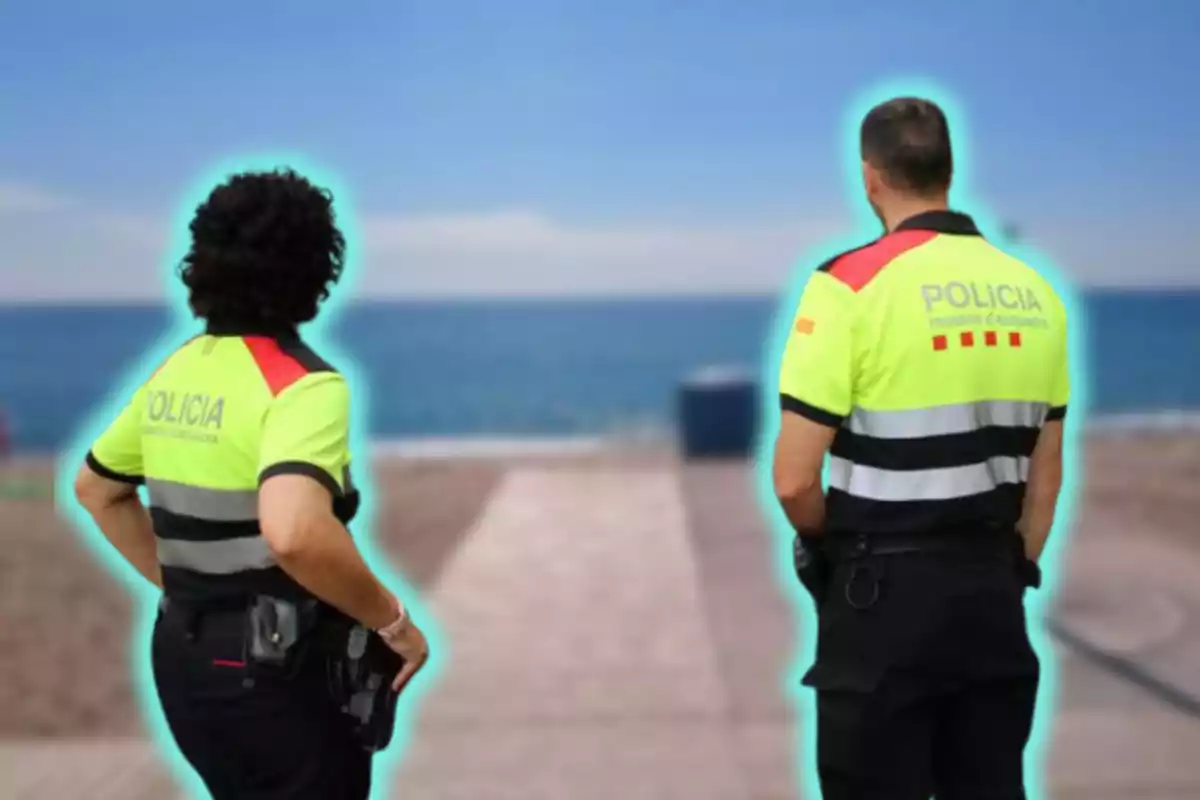 Dos policías de espaldas mirando hacia el mar en una playa.