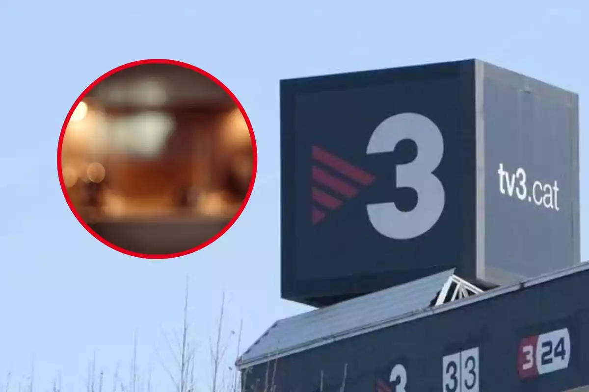 Un cartel grande de TV3 con el logo y la dirección web en un edificio bajo un cielo azul.