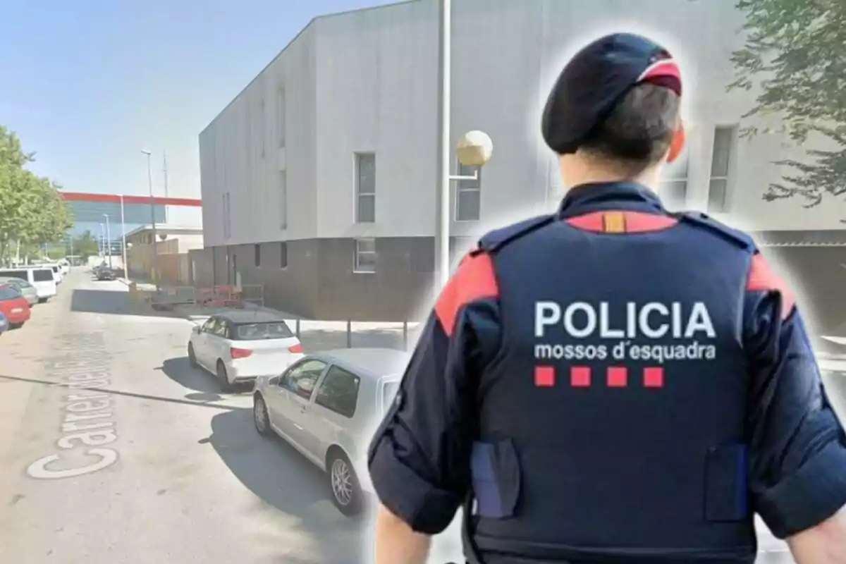 Un agente de los Mossos d'Esquadra de espaldas con uniforme de policía en una calle con varios coches estacionados y un edificio moderno al fondo.