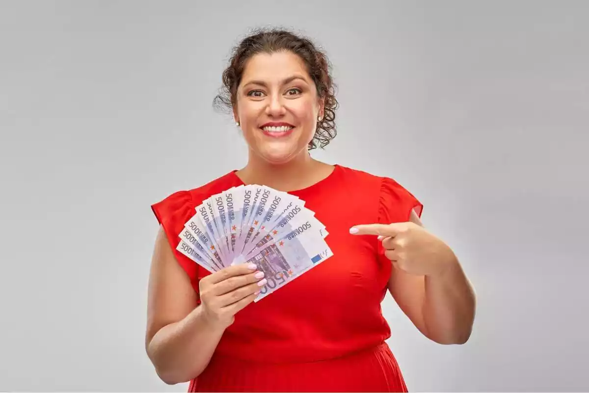 Una mujer sonriendo mientras señala a un fajo de billetes de 500 euros que tiene en su mano derecha