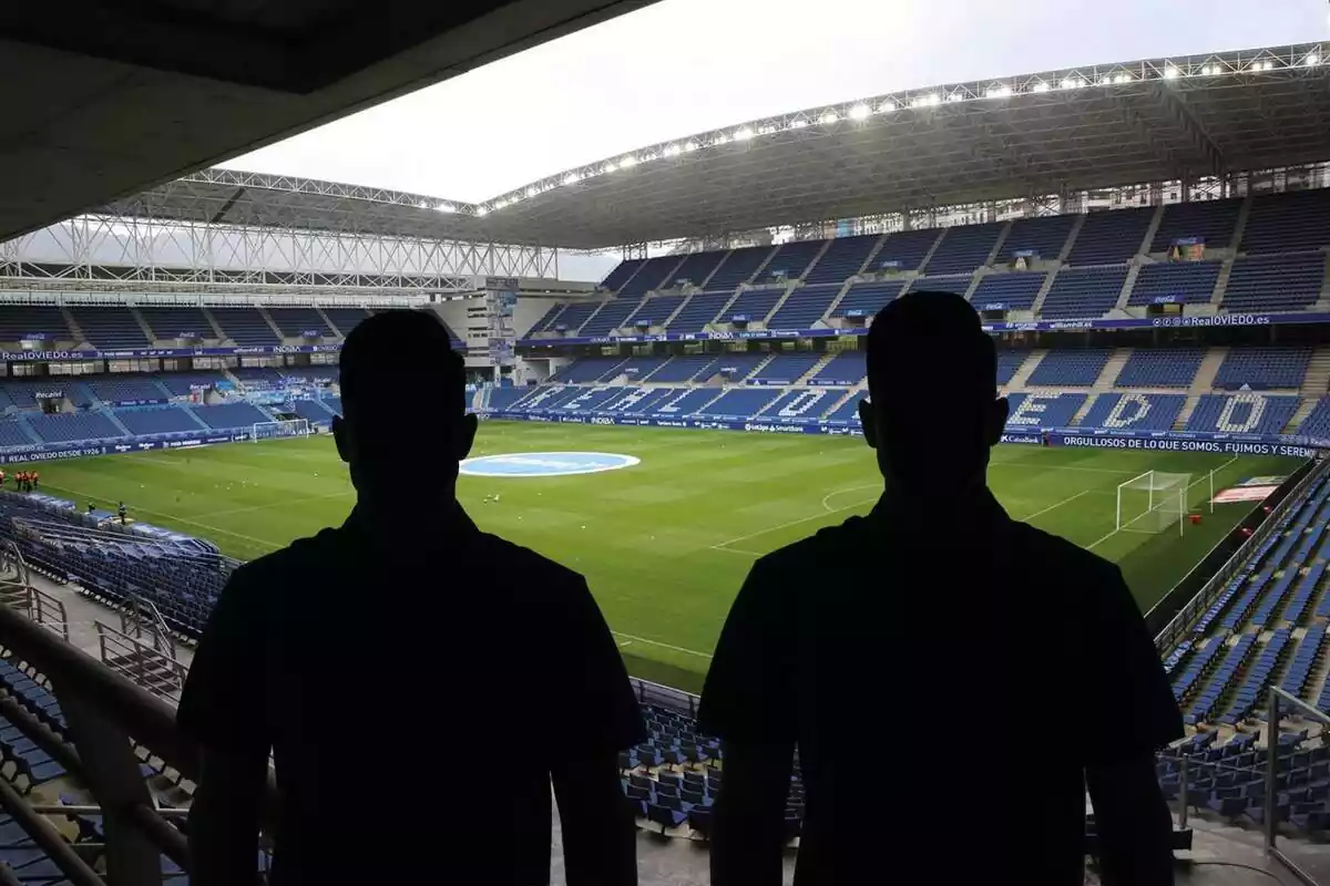 Montaje con una imagen del Carlos Tartiere, estadio del Real Oviedo, de fondo. En primer término dos sombras negras de hombre