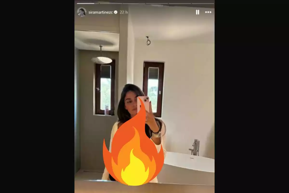 Una persona tomándose una selfie frente a un espejo en un baño, con un emoji de fuego cubriendo parte de su cuerpo.