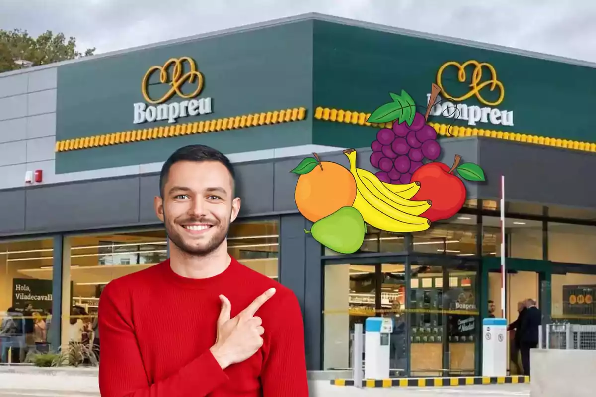 Un hombre sonriente con un suéter rojo señala hacia un grupo de frutas dibujadas frente a una tienda Bonpreu.