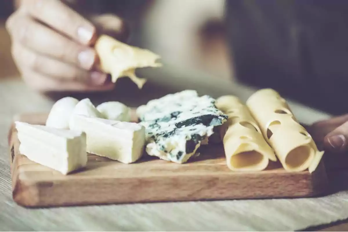 Una tabla de madera con varios tipos de queso y una mano sosteniendo un trozo de queso.