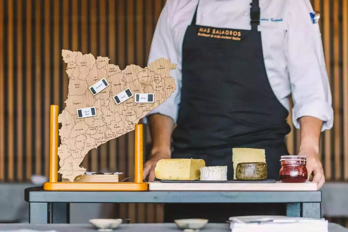 Imagen con un cocinero detrás de una tabla de quesos y un mapa de Catalunya