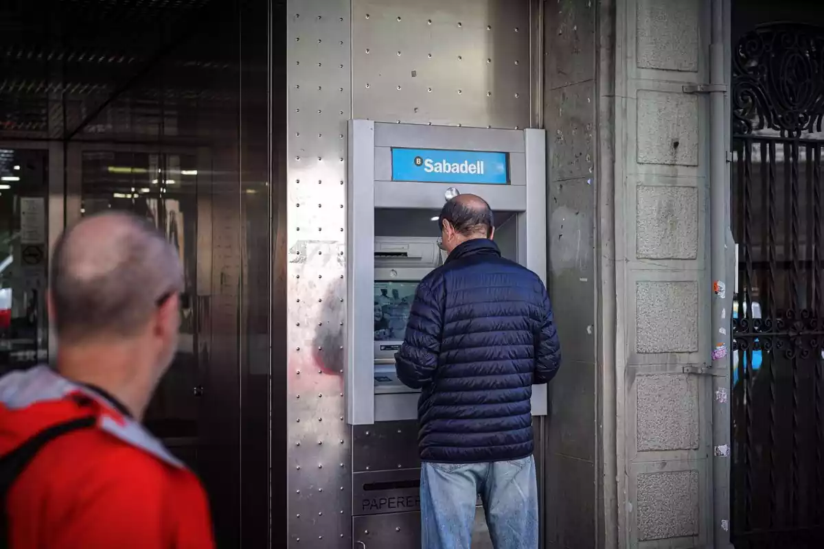 Un hombre de pie sacando dinero de un cajero del Banco Sabadell