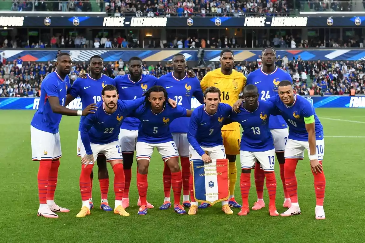 Jugadores de la selección de fútbol de Francia posando para una foto grupal en el campo antes de un partido contra Luxemburgo, con el público y el marcador de fondo.