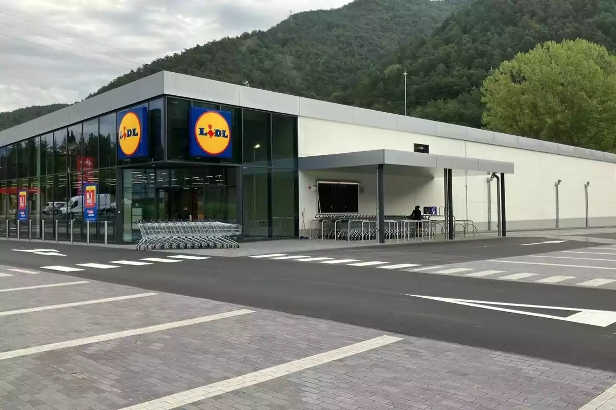 Fachada de un supermercado Lidl con carros de compra en la entrada y un entorno montañoso al fondo.