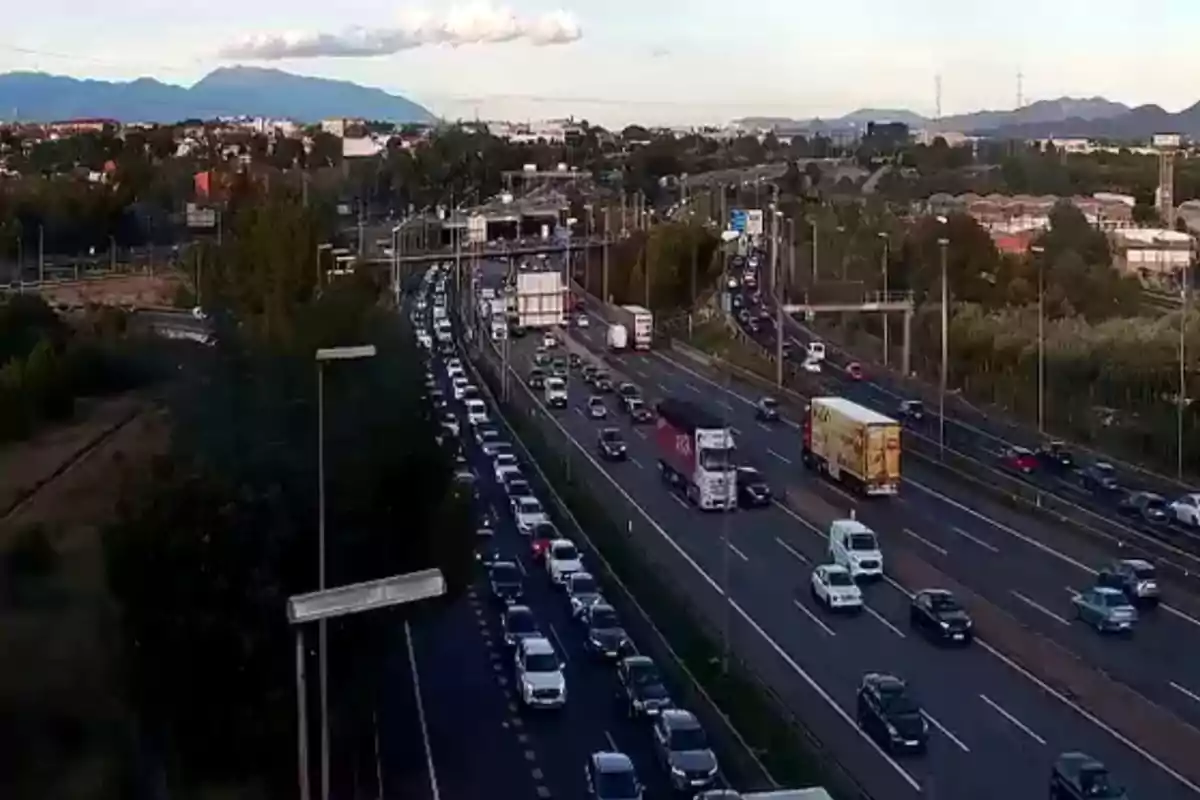 Una carretera con tráfico denso en ambos sentidos rodeada de árboles y montañas al fondo.